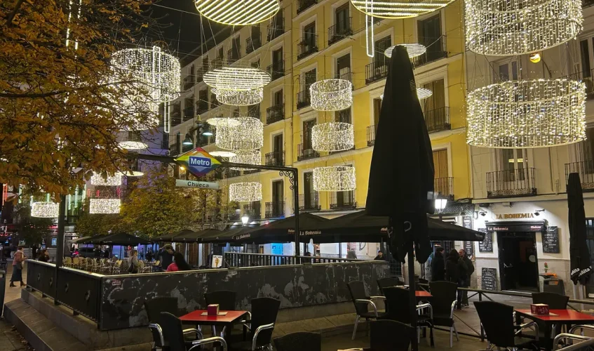 Luces navideñas y ambiente nocturno en la plaza de Chueca con la entrada del metro y terrazas al aire libre.