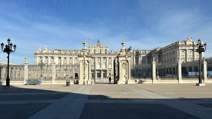 Palacio Real façade seen from the Plaza de la Armería, with the wrought-iron fence and a lone visitor in the courtyard, Madrid