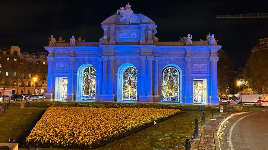 Puerta de Alcalá iluminada de noche con decoraciones navideñas y luz azul en su fachada.