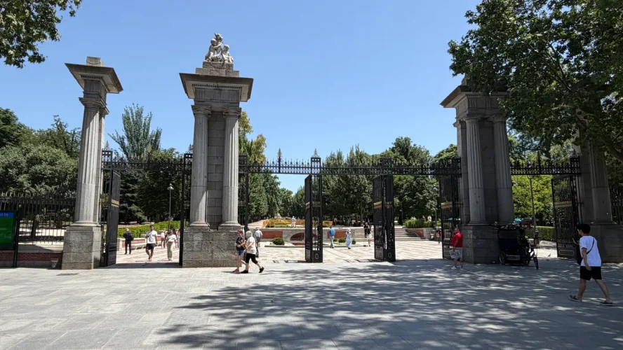 Puerta de la Independencia, the entrance gate to Parque del Retiro, Madrid, with the central archway open and visitors passing through.