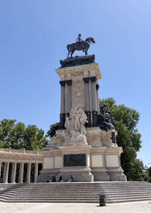 Three-quarter view of the Monumento a Alfonso XII, with the equestrian statue, allegorical sculptures, steps and part of the surrounding colonnade, in Parque del Retiro, Madrid.
